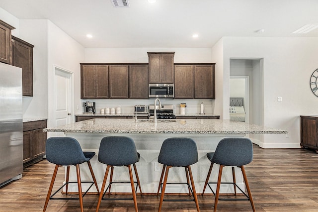 1818 Homewood Point Ln, Rosharon, TX 77583 - kitchen with a center island with sink, appliances with stainless steel finishes, a kitchen bar, dark wood-type flooring, and dark brown cabinetry