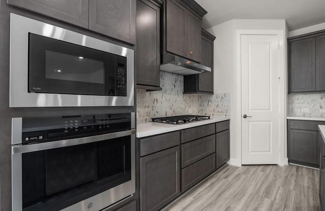 7827 Albury Mnr, Richmond, TX 77407 - kitchen featuring stainless steel appliances, light countertops, light wood finished floors, backsplash, and under cabinet range hood