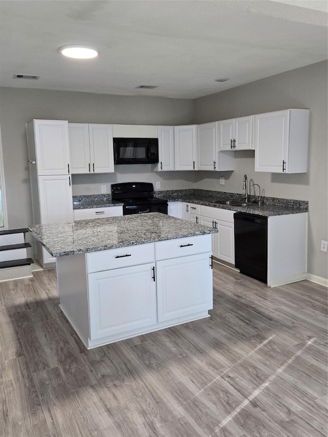 204 Jasmine St, Lake Jackson, TX 77566 - kitchen with black appliances, a center island, white cabinetry, light stone counters, and light wood-style floors