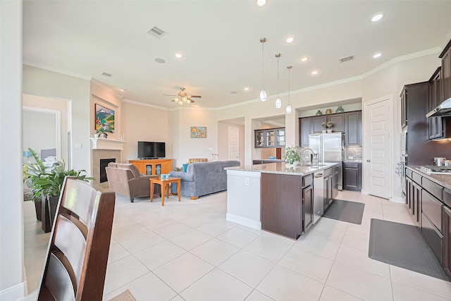 25603 Kearsley Dr, Katy, TX 77494 - kitchen featuring dark brown cabinets, an island with sink, light stone countertops, crown molding, and a ceiling fan
