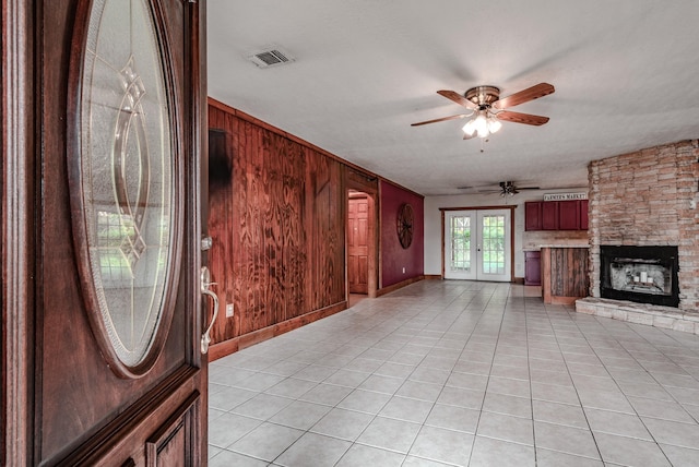 521 Northwood Dr, Point Blank, TX 77364 - unfurnished living room with wooden walls, light tile patterned flooring, ceiling fan, french doors, and a stone fireplace