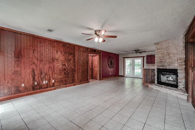 521 Northwood Dr, Point Blank, TX 77364 - unfurnished living room featuring ceiling fan, wood walls, a stone fireplace, a textured ceiling, and light tile patterned floors