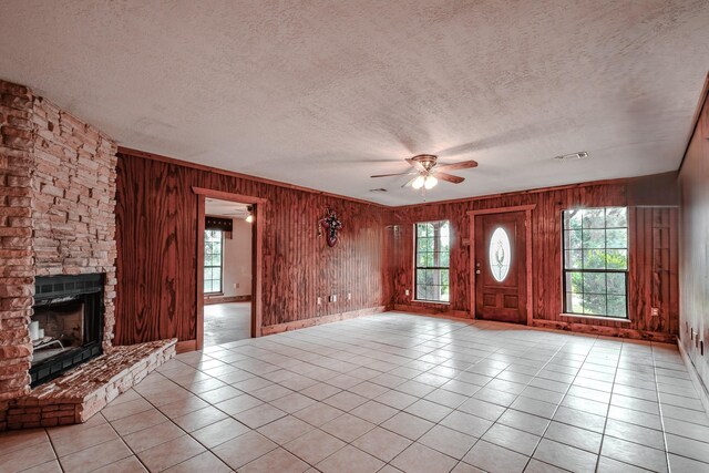 521 Northwood Dr, Point Blank, TX 77364 - unfurnished living room featuring ceiling fan, light tile patterned floors, wooden walls, a textured ceiling, and a stone fireplace