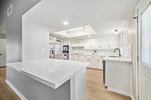 3114 Wagon Trail Dr, Sugar Land, TX 77479 - kitchen featuring black appliances, light wood-style flooring, a peninsula, white cabinets, and a skylight