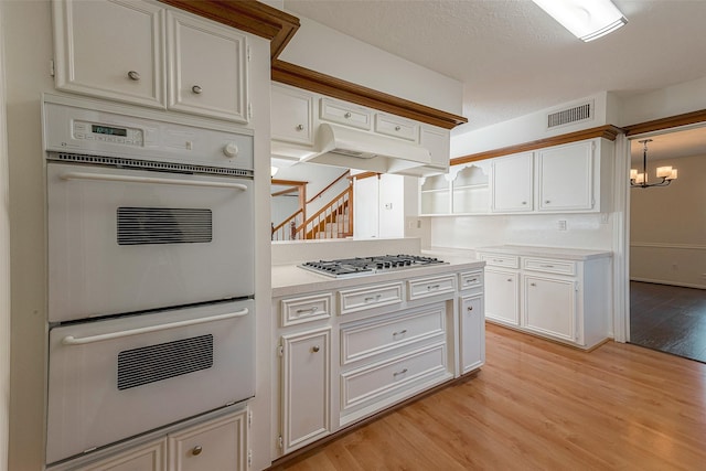 2510 Wind Fall Ln, Sugar Land, TX 77479 - kitchen with white double oven, stainless steel gas cooktop, light wood-style flooring, light countertops, and white cabinetry