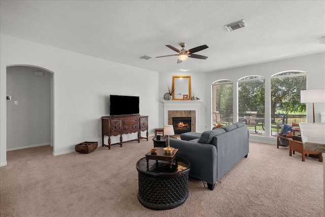 1427 Roaring Springs Ln, Seabrook, TX 77586 - living room with light colored carpet, ceiling fan, arched walkways, a tile fireplace, and a textured ceiling