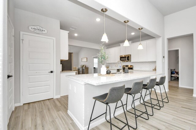 8419 Sunset Horizon Dr, Baytown, TX 77521 - kitchen with stainless steel microwave, white cabinetry, light wood-style floors, a breakfast bar area, and recessed lighting