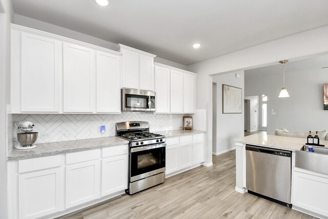 8419 Sunset Horizon Dr, Baytown, TX 77521 - kitchen featuring appliances with stainless steel finishes, backsplash, white cabinetry, hanging light fixtures, and light wood-type flooring