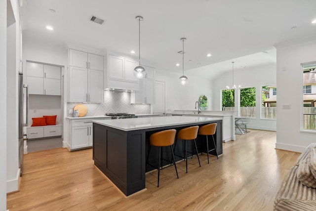 5216 Chestnut St, Bellaire, TX 77401 - kitchen with light countertops, decorative backsplash, a breakfast bar area, white cabinets, and light wood-style flooring
