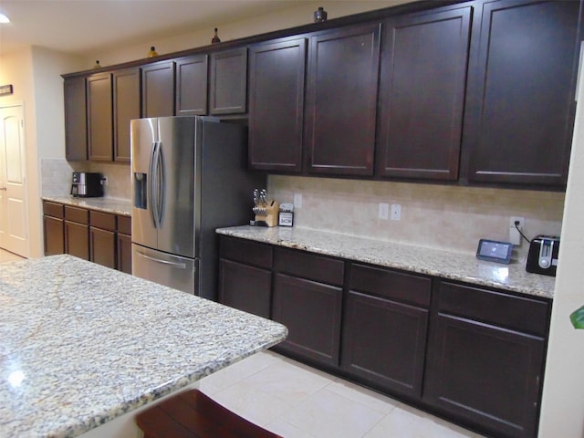 23727 Scotsman Dr, Katy, TX 77493 - kitchen featuring stainless steel fridge with ice dispenser, backsplash, dark brown cabinetry, light stone countertops, and light tile patterned floors