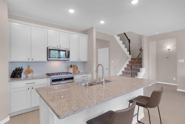 31319 Mallet Cv, Fulshear, TX 77441 - kitchen with appliances with stainless steel finishes, light wood-style floors, backsplash, white cabinets, and a center island with sink