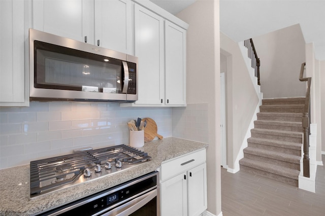 31319 Mallet Cv, Fulshear, TX 77441 - kitchen with stainless steel appliances, white cabinets, decorative backsplash, light wood finished floors, and light stone countertops