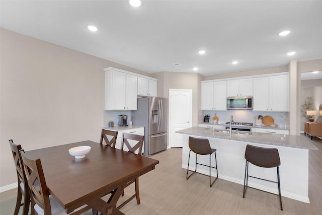 31319 Mallet Cv, Fulshear, TX 77441 - kitchen featuring stainless steel appliances, decorative backsplash, a kitchen bar, a kitchen island with sink, and white cabinets