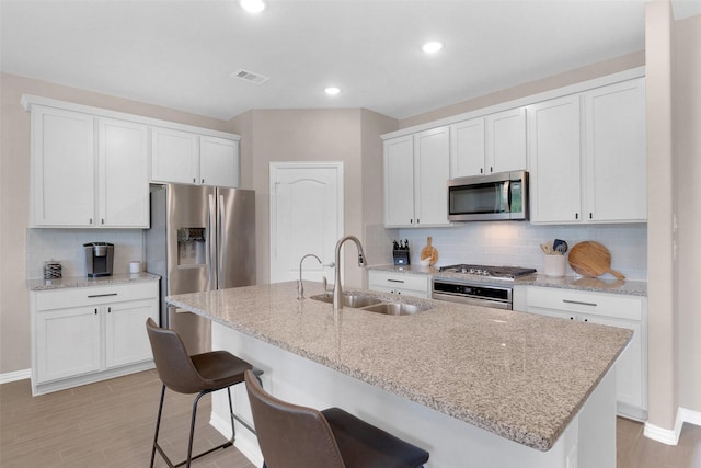 31319 Mallet Cv, Fulshear, TX 77441 - kitchen featuring stainless steel appliances, backsplash, light wood-style floors, white cabinets, and an island with sink