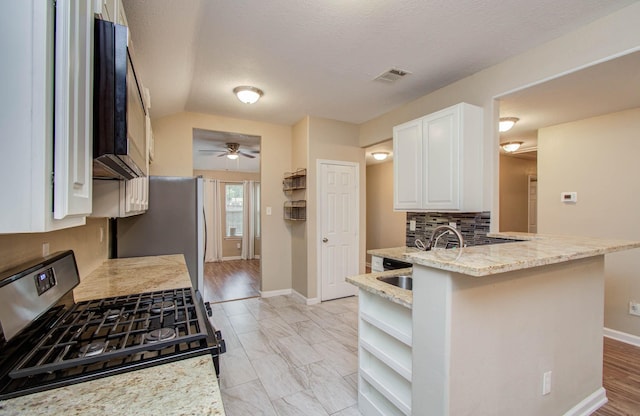 5409 Gold St, Houston, TX 77026 - kitchen with stainless steel appliances, white cabinetry, light stone counters, ceiling fan, and tasteful backsplash