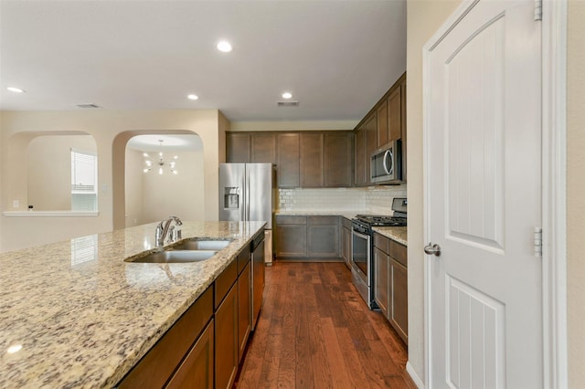 24030 Tirso River Ct, Katy, TX 77493 - kitchen with stainless steel appliances, a chandelier, arched walkways, dark wood-type flooring, and light stone counters