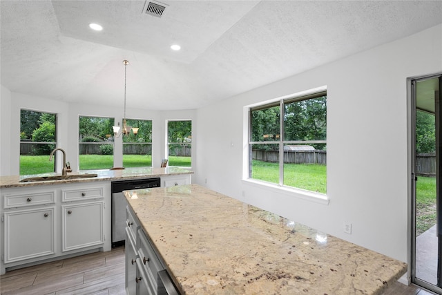 2403 Mustang Dr, Conroe, TX 77384 - kitchen featuring stainless steel dishwasher, healthy amount of natural light, a textured ceiling, light stone countertops, and light wood finished floors