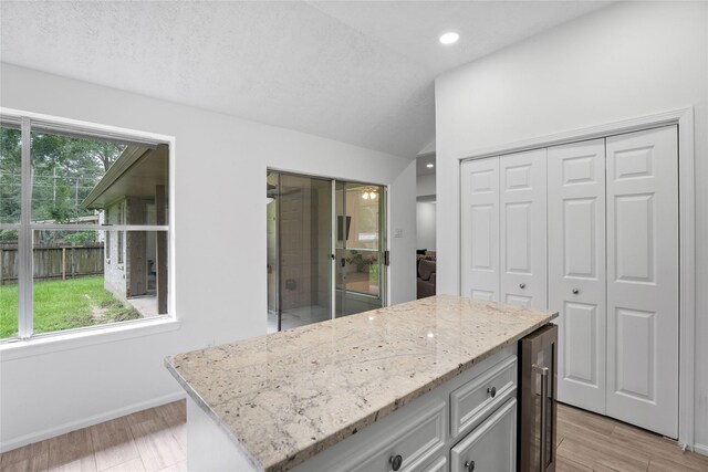 2403 Mustang Dr, Conroe, TX 77384 - kitchen with wine cooler, light stone counters, lofted ceiling, light wood-type flooring, and a center island