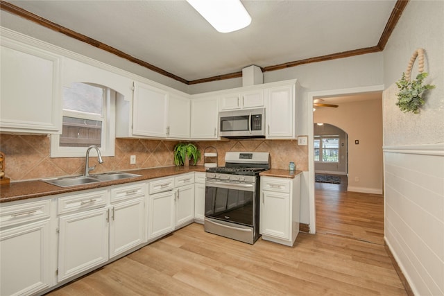 911 Wooding St, Houston, TX 77011 - kitchen featuring appliances with stainless steel finishes, arched walkways, light wood-type flooring, ornamental molding, and white cabinets