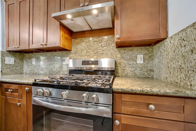 21614 Bowcreek Ln, Katy, TX 77449 - kitchen with gas stove, under cabinet range hood, decorative backsplash, brown cabinetry, and light stone countertops