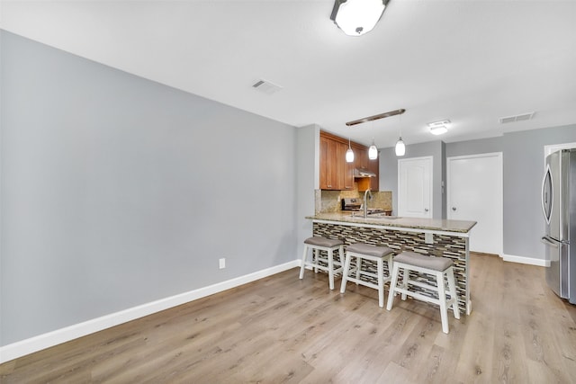 21614 Bowcreek Ln, Katy, TX 77449 - kitchen featuring freestanding refrigerator, light wood finished floors, a peninsula, tasteful backsplash, and a breakfast bar area