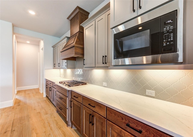 3242 N Upland St, Katy, TX 77493 - kitchen with appliances with stainless steel finishes, light wood finished floors, decorative backsplash, light stone counters, and custom range hood