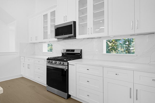 2122 Oatfield Dr, Houston, TX 77018 - kitchen with stainless steel appliances, decorative backsplash, white cabinetry, light wood-style floors, and glass insert cabinets