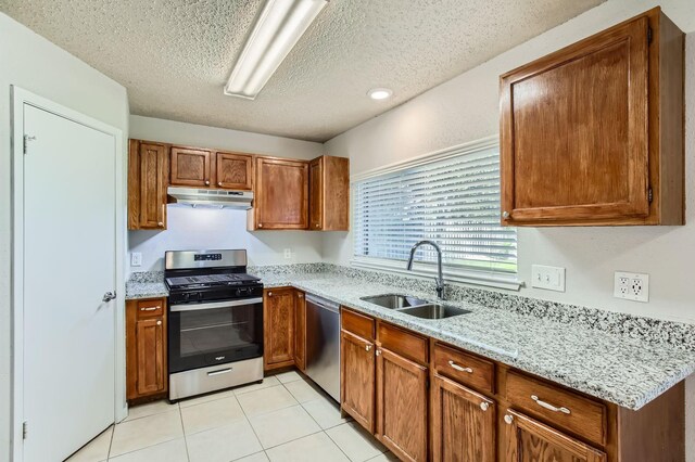 11910 Yearling Dr, Houston, TX 77065 - kitchen featuring stainless steel appliances, under cabinet range hood, brown cabinetry, a textured ceiling, and light stone countertops