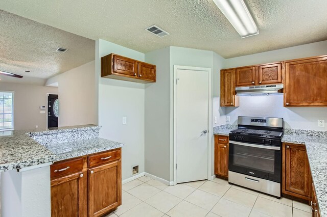 11910 Yearling Dr, Houston, TX 77065 - kitchen with stainless steel gas range, under cabinet range hood, a textured ceiling, brown cabinetry, and light tile patterned flooring