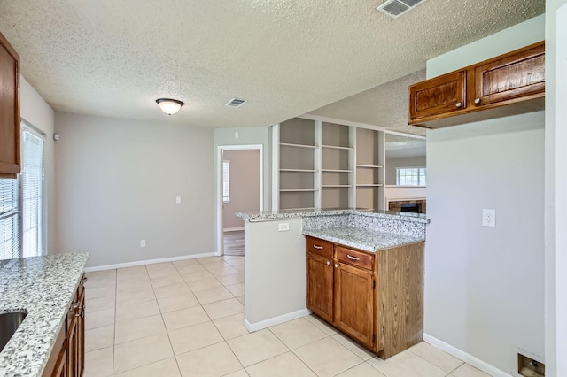 11910 Yearling Dr, Houston, TX 77065 - kitchen with light stone counters, a textured ceiling, light tile patterned flooring, a fireplace, and brown cabinetry