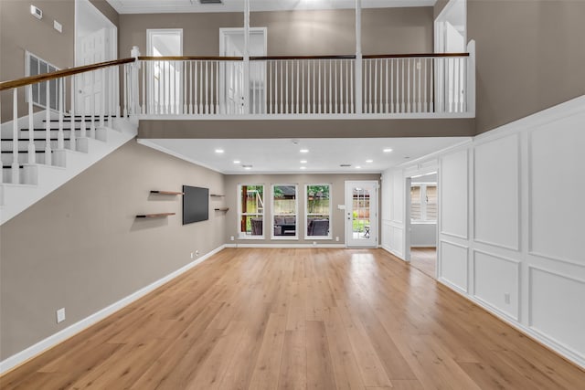 17427 Pinewood Forest Dr, Spring, TX 77379 - unfurnished living room featuring a decorative wall, light wood-style flooring, stairs, ornamental molding, and a towering ceiling