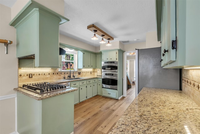 17427 Pinewood Forest Dr, Spring, TX 77379 - kitchen with stainless steel appliances, green cabinets, backsplash, light wood-style flooring, and light stone countertops