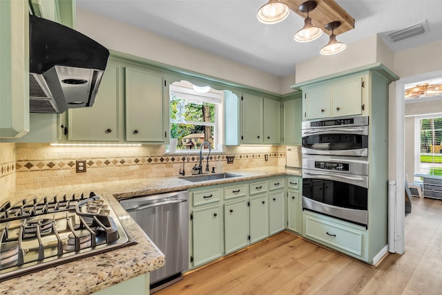 17427 Pinewood Forest Dr, Spring, TX 77379 - kitchen with stainless steel appliances, exhaust hood, green cabinetry, light wood finished floors, and tasteful backsplash