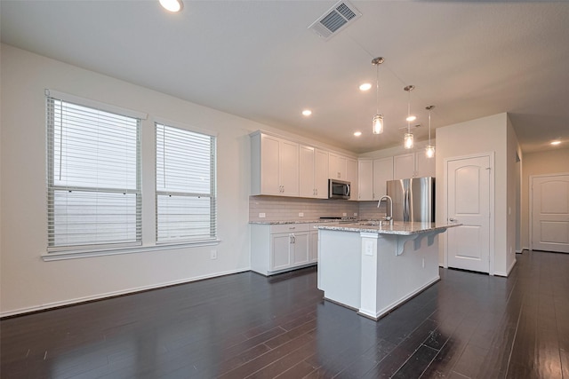 3414 Signor Dr, Houston, TX 77025 - kitchen with appliances with stainless steel finishes, white cabinets, light stone countertops, dark wood-type flooring, and a kitchen island with sink