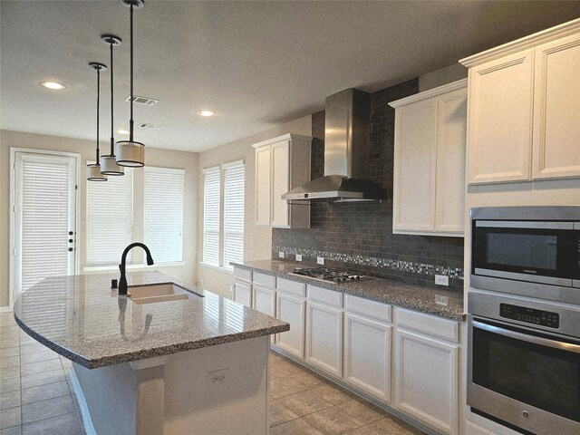 3811 Pearl Pass Ln, Sugar Land, TX 77479 - kitchen with appliances with stainless steel finishes, wall chimney range hood, light tile patterned floors, decorative backsplash, and a kitchen island with sink