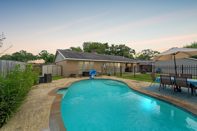 11614 Brighton Ln, Meadows Place, TX 77477 - pool at dusk featuring a storage unit, a fenced backyard, and a patio area