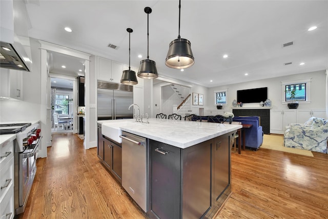 811 Byrne St, Houston, TX 77009 - kitchen with premium appliances, wall chimney range hood, light wood-style floors, a fireplace, and an island with sink