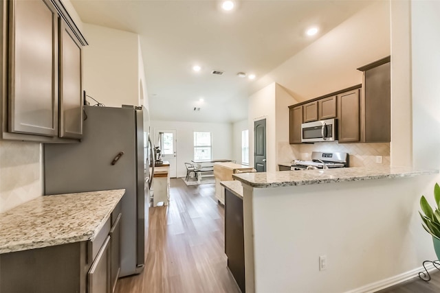 16107 Dockside St, Crosby, TX 77532 - kitchen with appliances with stainless steel finishes, decorative backsplash, wood finished floors, vaulted ceiling, and light stone counters