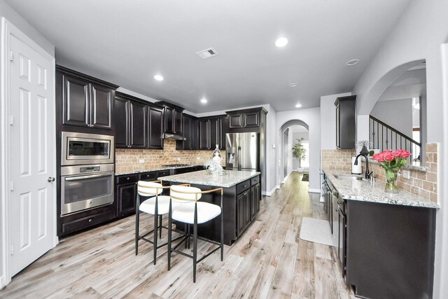 9003 Alps Peak Ct, Richmond, TX 77407 - kitchen with appliances with stainless steel finishes, arched walkways, backsplash, light wood-type flooring, and a kitchen island