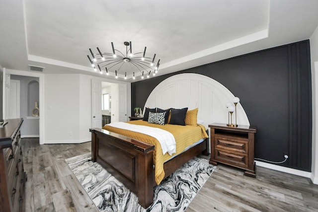 9003 Alps Peak Ct, Richmond, TX 77407 - bedroom featuring a raised ceiling, wood finished floors, a chandelier, and connected bathroom