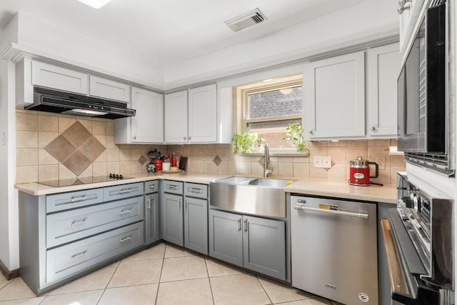 9611 Stockport Dr, Spring, TX 77379 - kitchen with appliances with stainless steel finishes, under cabinet range hood, gray cabinets, light countertops, and light tile patterned floors