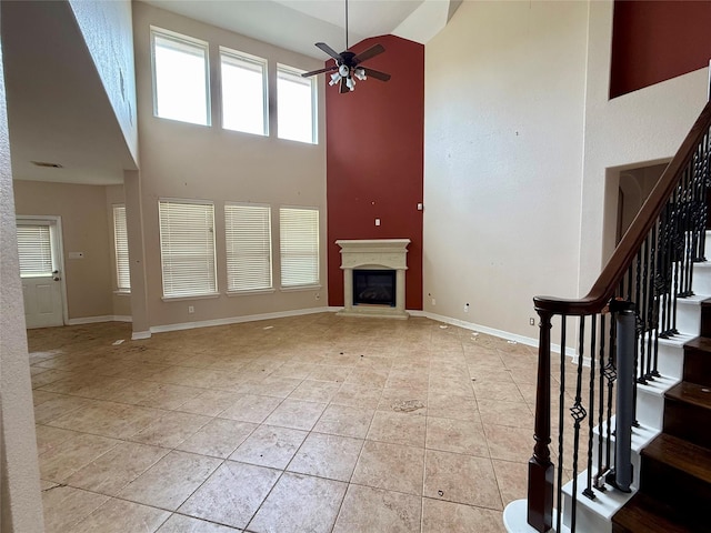 12503 Pepper Creek Ln, Pearland, TX 77584 - unfurnished living room with a towering ceiling, a ceiling fan, light tile patterned floors, stairway, and a glass covered fireplace