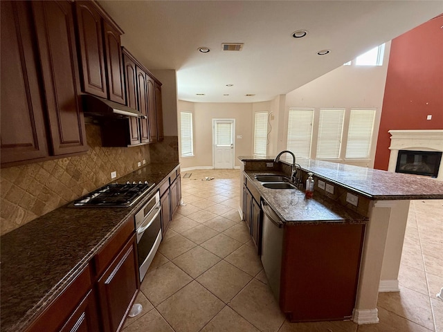 12503 Pepper Creek Ln, Pearland, TX 77584 - kitchen with appliances with stainless steel finishes, light tile patterned flooring, backsplash, under cabinet range hood, and an island with sink