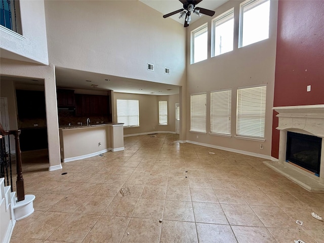 12503 Pepper Creek Ln, Pearland, TX 77584 - unfurnished living room with ceiling fan, a towering ceiling, healthy amount of natural light, a glass covered fireplace, and light tile patterned floors