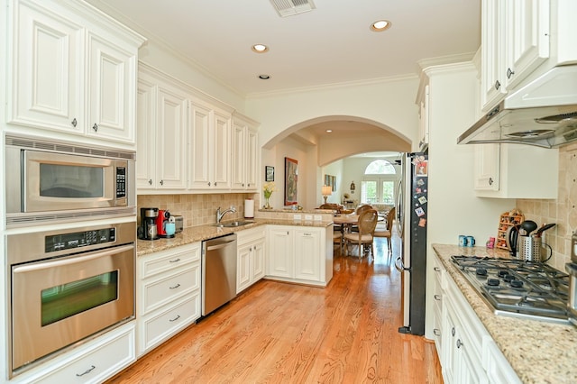 1307 W Bell St, Houston, TX 77019 - kitchen featuring stainless steel appliances, arched walkways, decorative backsplash, light wood-style flooring, and recessed lighting