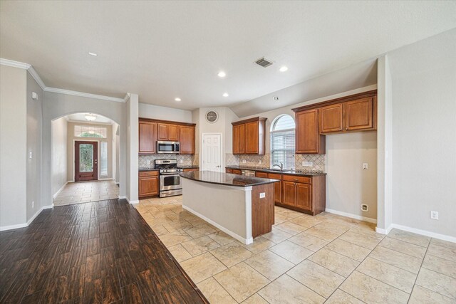 20779 Oakhurst Meadows Dr, Porter, TX 77365 - kitchen with stainless steel appliances, arched walkways, backsplash, brown cabinetry, and ornamental molding