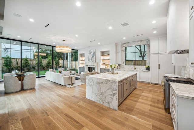 2220 Pelham Dr, Houston, TX 77019 - kitchen featuring gas range, premium range hood, light wood-style flooring, open floor plan, and light stone counters