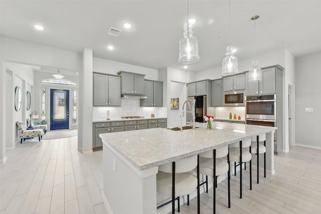 250 Peninsula Point Dr, Montgomery, TX 77356 - kitchen with gray cabinetry, appliances with stainless steel finishes, backsplash, a breakfast bar, and a large island with sink