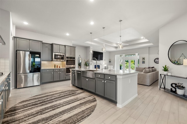 250 Peninsula Point Dr, Montgomery, TX 77356 - kitchen with stainless steel appliances, gray cabinets, a tray ceiling, open floor plan, and light wood-style flooring