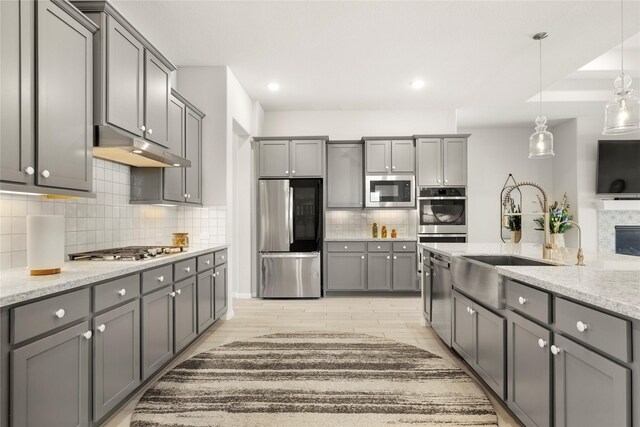 250 Peninsula Point Dr, Montgomery, TX 77356 - kitchen with stainless steel appliances, gray cabinets, under cabinet range hood, tasteful backsplash, and light stone counters